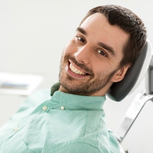 Man in green shirt smiling while sitting in dental chair