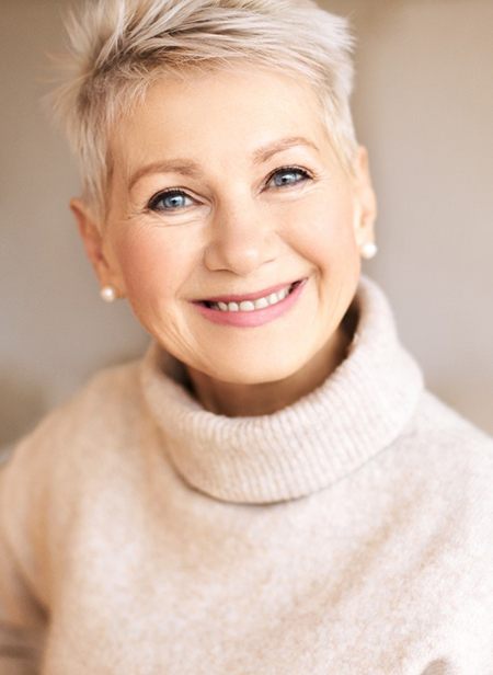 An older woman wearing a cream-colored sweater and showing off her new smile thanks to dentures in Manchester