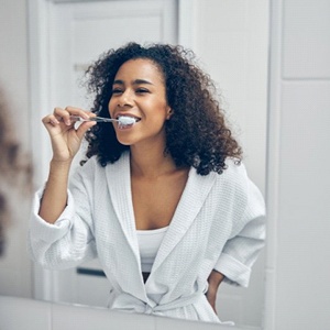 woman in a bathrobe brushing her teeth in front of a mirror