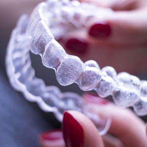 Fingers with red nail polish holding Invisalign trays