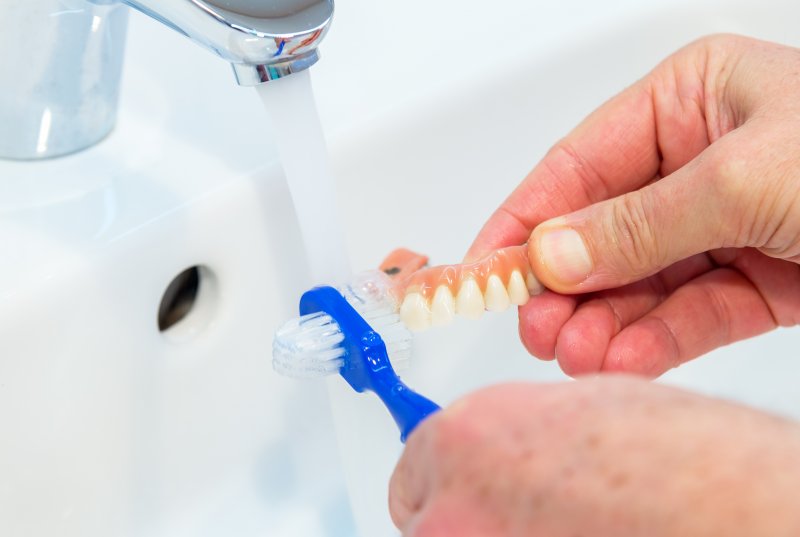 a person using a denture brush to clean their full denture 