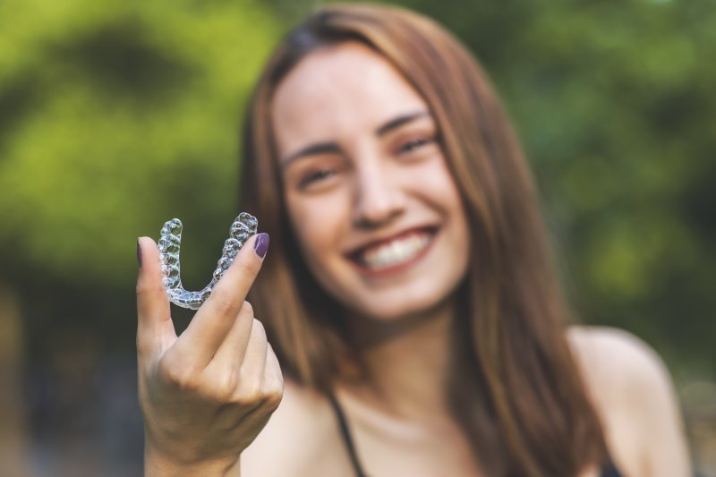 a young woman holding an Invisalign aligner and smiling 