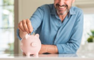 man putting coins into a pink piggy bank 