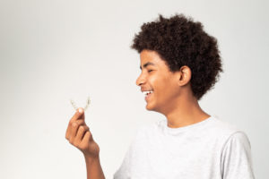 a teen holding their Invisalign aligners and smiling