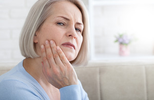 Woman rubbing her jaw looking concerned