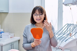 Female dental patient holding mirror to check smile