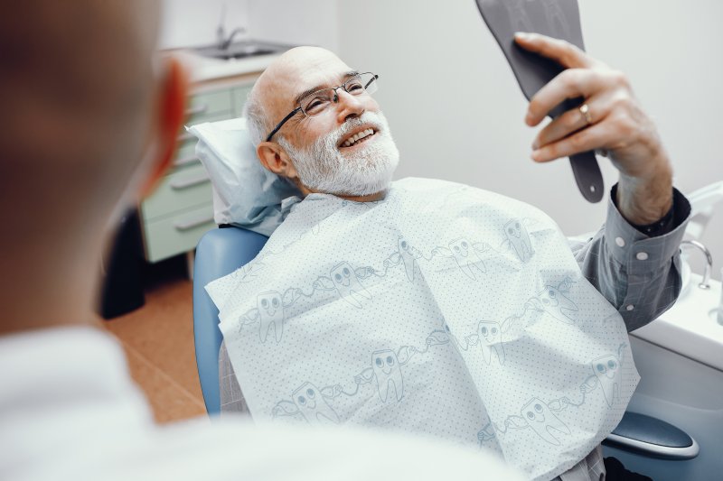An older man admiring his implant dentures with a hand mirror