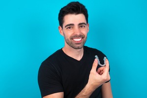 Man in black shirt holding an Invisalign aligner
